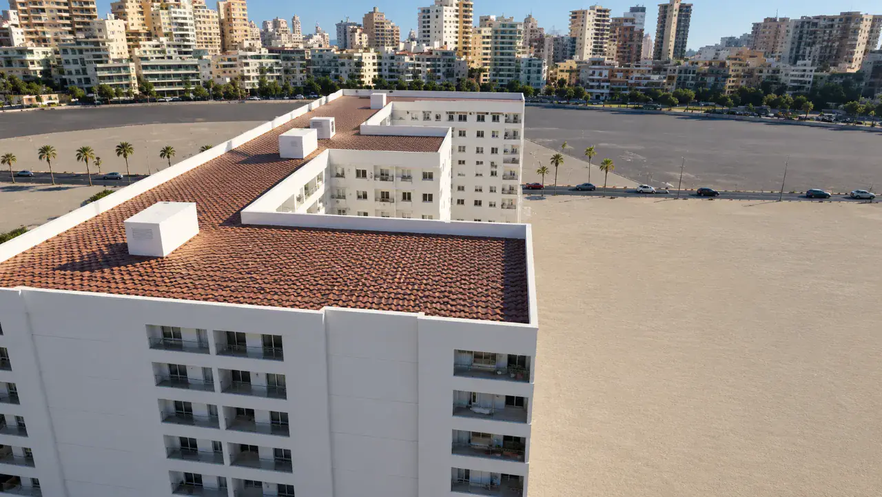 Vue du ciel : toiture et façades blanches de la résidence, avec les immeubles du centre-ville d'Agadir en arrière-plan